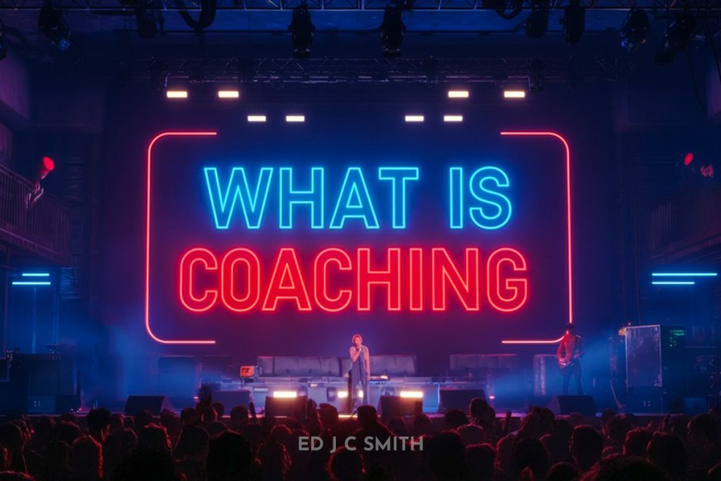 What Is Coaching - A person on stage addressing an audience with a large neon sign displaying the words "What Is Coaching" in blue and red lights.